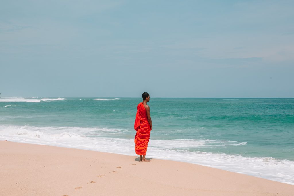 A monk in contemplation at the edge of the vast ocean, seeking to break curses through spiritual enlightenment.