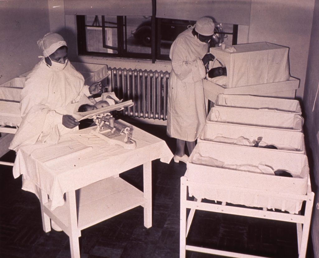 Babies ward in a hospital. Filled with babies and two medical practitioners attending to the babies.